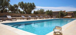 Una piscina con sillones de descanso y un tarro de vidrio en el borde.