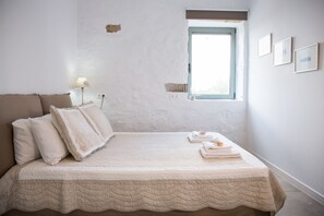 Un dormitorio con cama, almohadas, una ventana y una lámpara fijada a la pared.