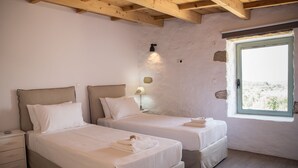 Ein Schlafzimmer mit zwei Betten, Holzbalken an der Decke, einem Nachttisch, einer Lampe und einem Fenster mit Blick.