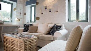 Ein gemütliches Wohnzimmer mit einem weißen Sofa, gemusterten Kissen, einem Holztisch und Blick durch ein Fenster.