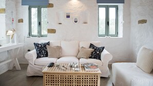Ein raumheller Raum mit einem weißen Sofa, einem Holztisch und zwei Fenstern mit blauen Fensterläden.