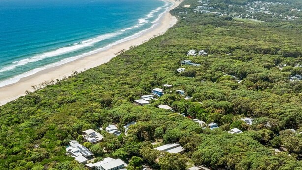An aerial view of a coastal area with a beach and a cluster of houses surrounded by dense greenery. - 16 Ibis Court - Rainbow Shores. Wifi. Pool. Quick walk to beach (RAINBOW BEACH)