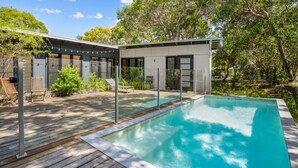 A modern outdoor pool area with a wooden deck, a covered seating area, and a glass-enclosed structure. - 16 Ibis Court - Rainbow Shores. Wifi. Pool. Quick walk to beach (RAINBOW BEACH)