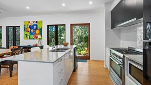 A modern kitchen with a central island, stainless steel appliances, and large windows offering views of greenery. - 16 Ibis Court - Rainbow Shores. Wifi. Pool. Quick walk to beach (RAINBOW BEACH)
