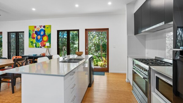 A modern kitchen with a central island, stainless steel appliances, and large windows offering views of greenery.