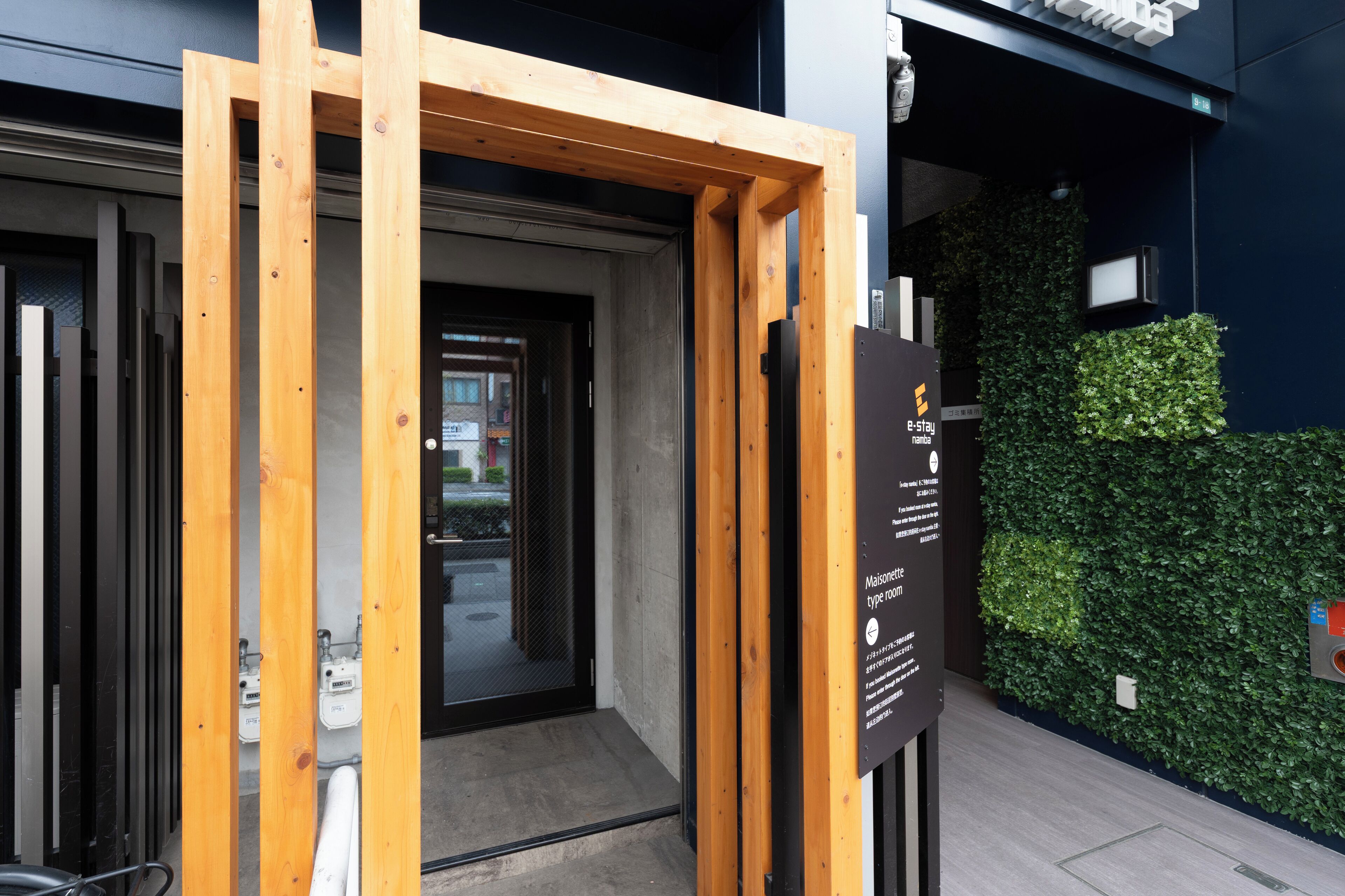 Een hotelentree met een houten frame, een glazen deur en een groene wand met een verticale tuin.