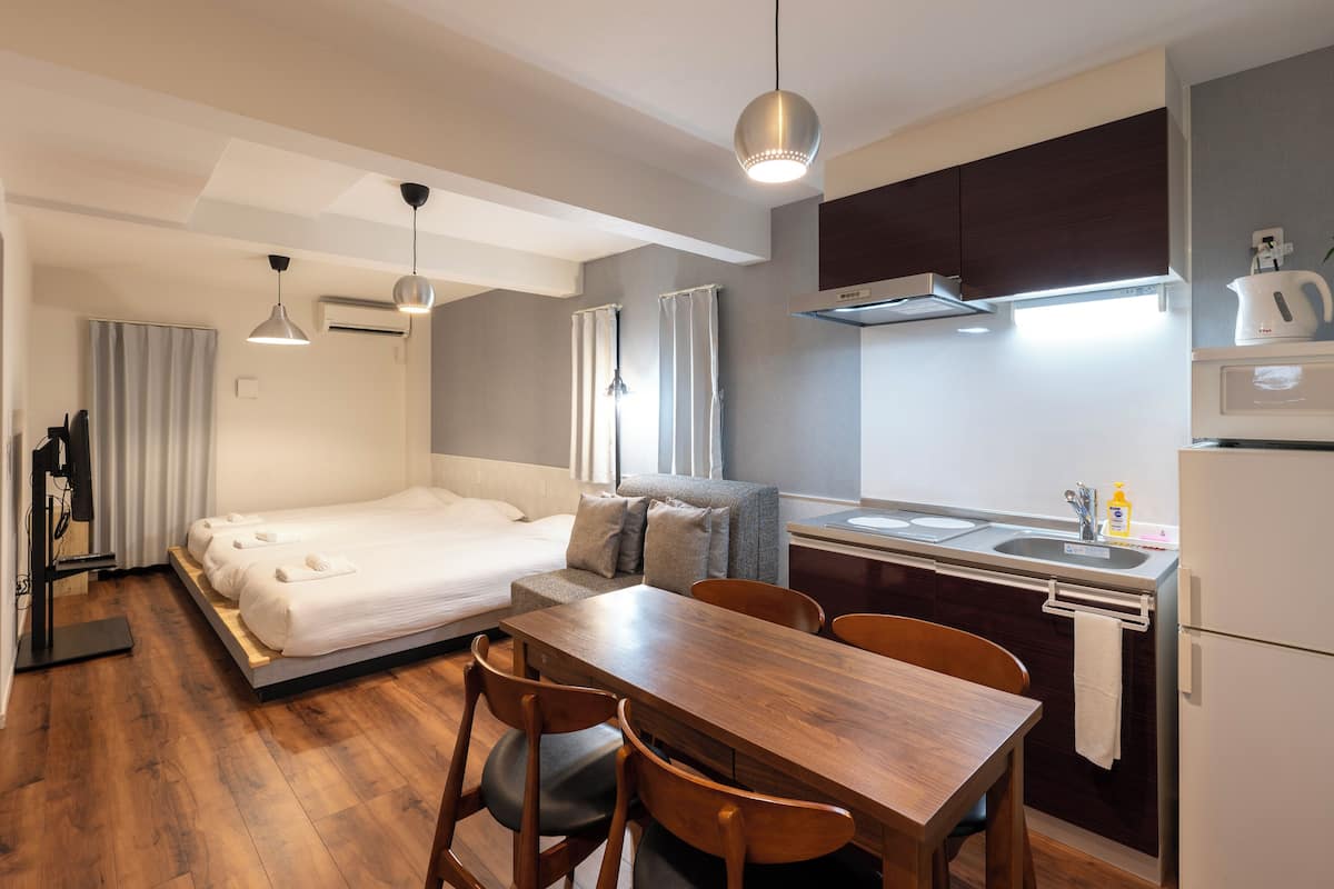 Una habitación de hotel compacta con cama, un pequeño sofá, una mesa de comedor y una kitchenette.
