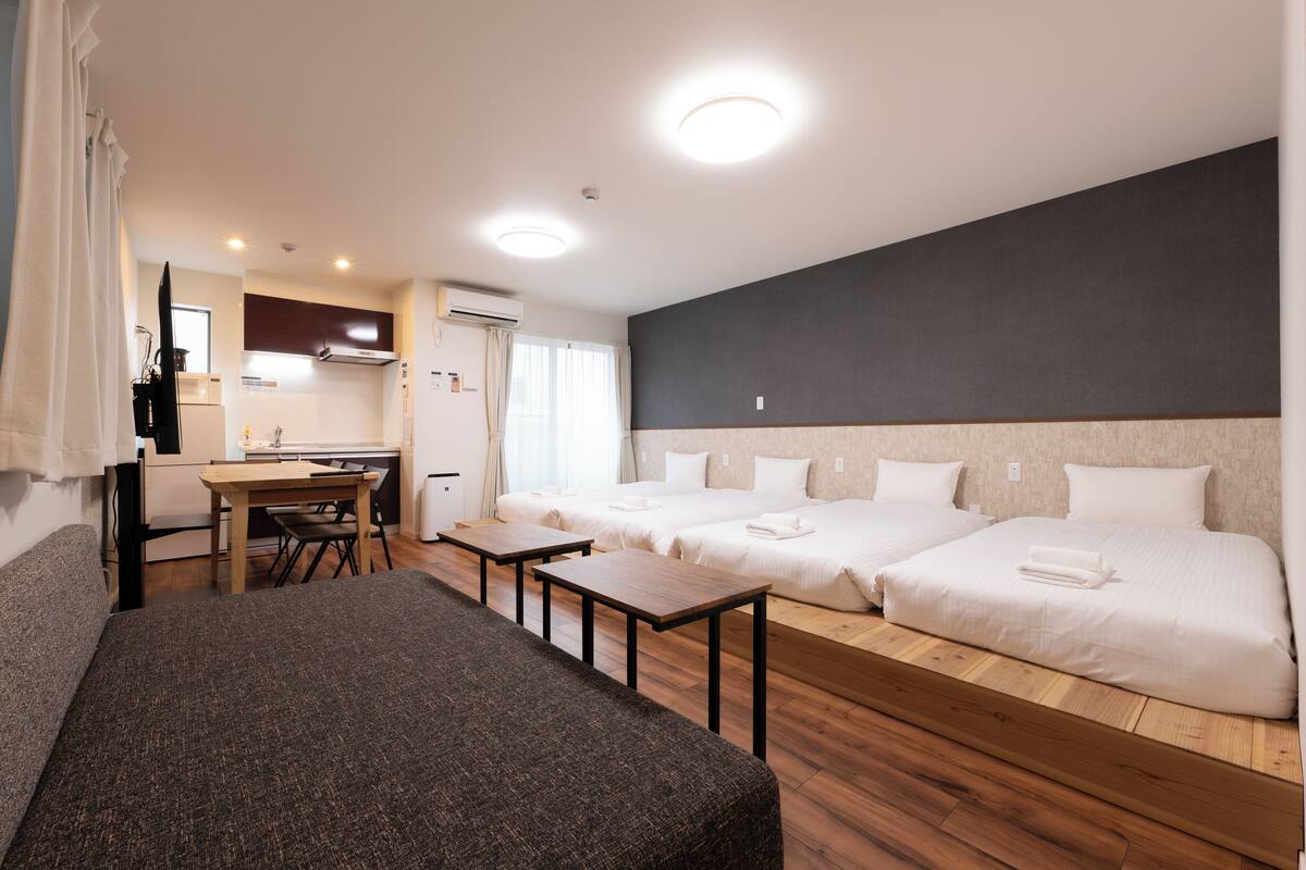Una habitación de hotel con sofá, dos camas, una mesa de comedor y una zona de cocina.