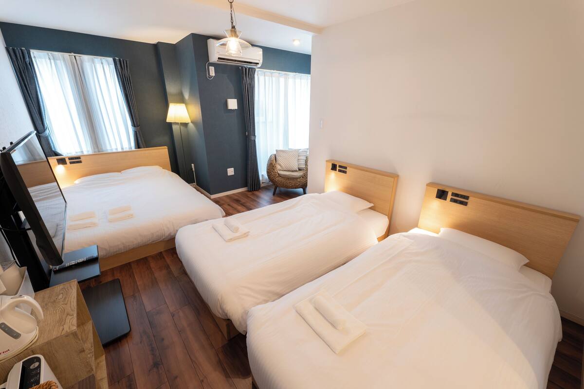 Habitación de hotel con dos camas, un escritorio con computadora, una silla y un ventanal con cortinas.