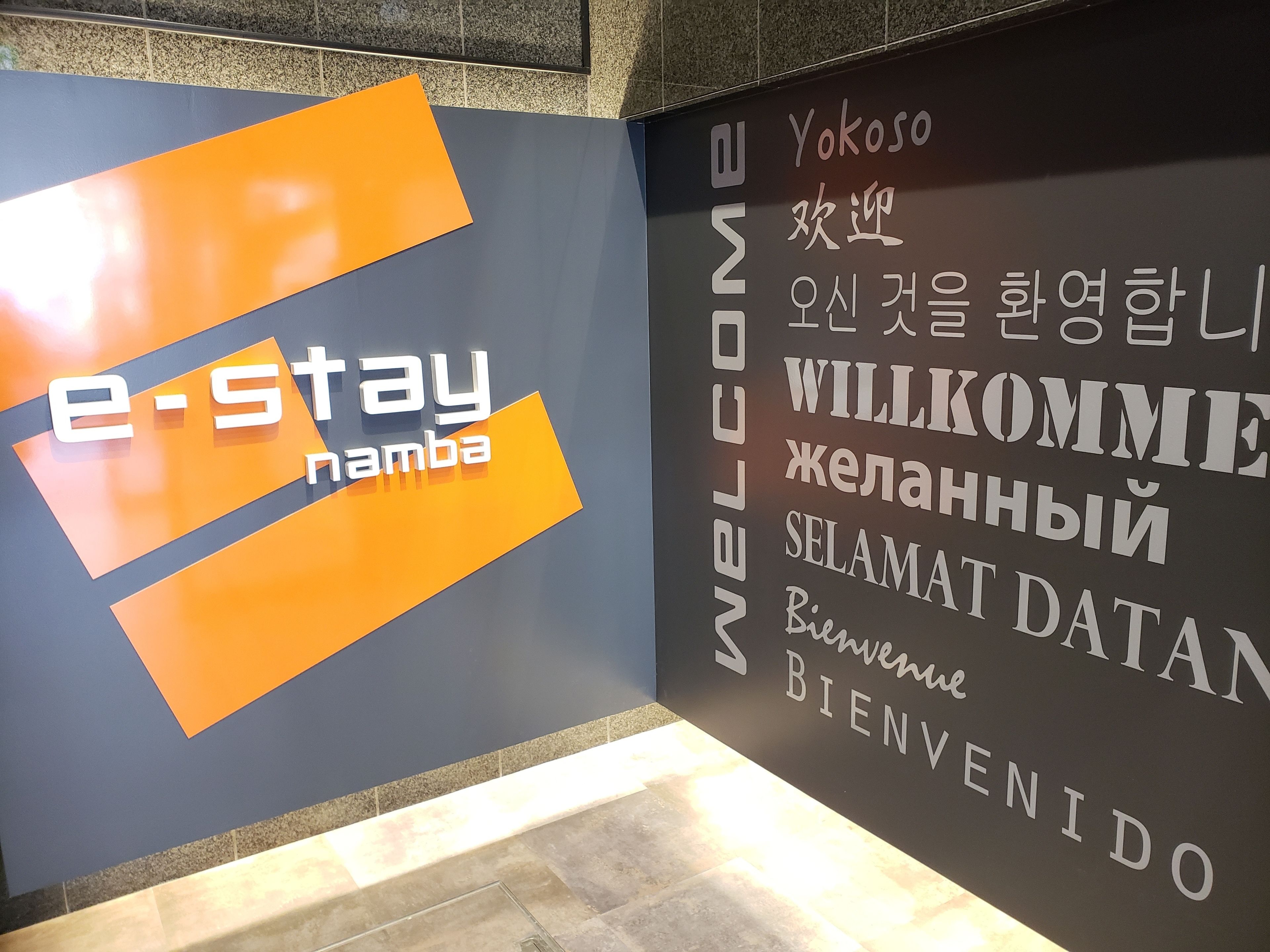 A wall with a sign that reads "e-Stay namba" and "WELCOME" in multiple languages.