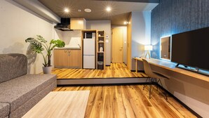 A modern living room with a wooden floor, a sofa, a TV, and a potted plant.