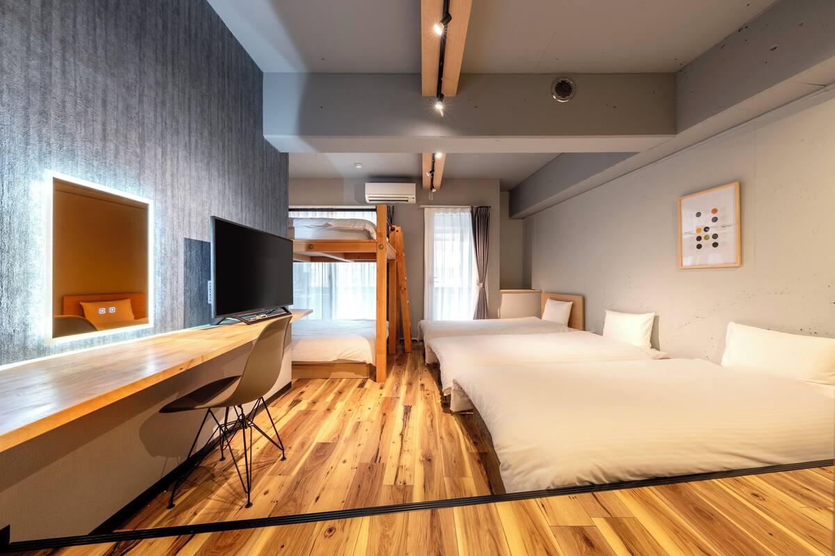 Una habitación de hotel moderna con piso de madera, un escritorio con silla, una cama individual sobre otra, un televisor y un cuadro enmarcado en la pared.