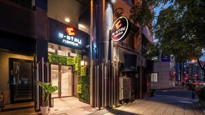 A modern building with a glass entrance, a sign for 'e-stay namba', and a vertical garden on the side.