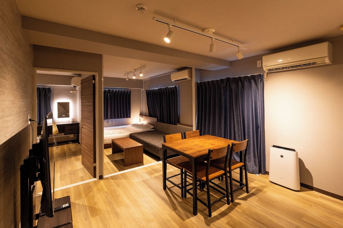 Una habitación de hotel moderna con una mesa de comedor de madera, un sofá, un escritorio con un ordenador y un aire acondicionado.