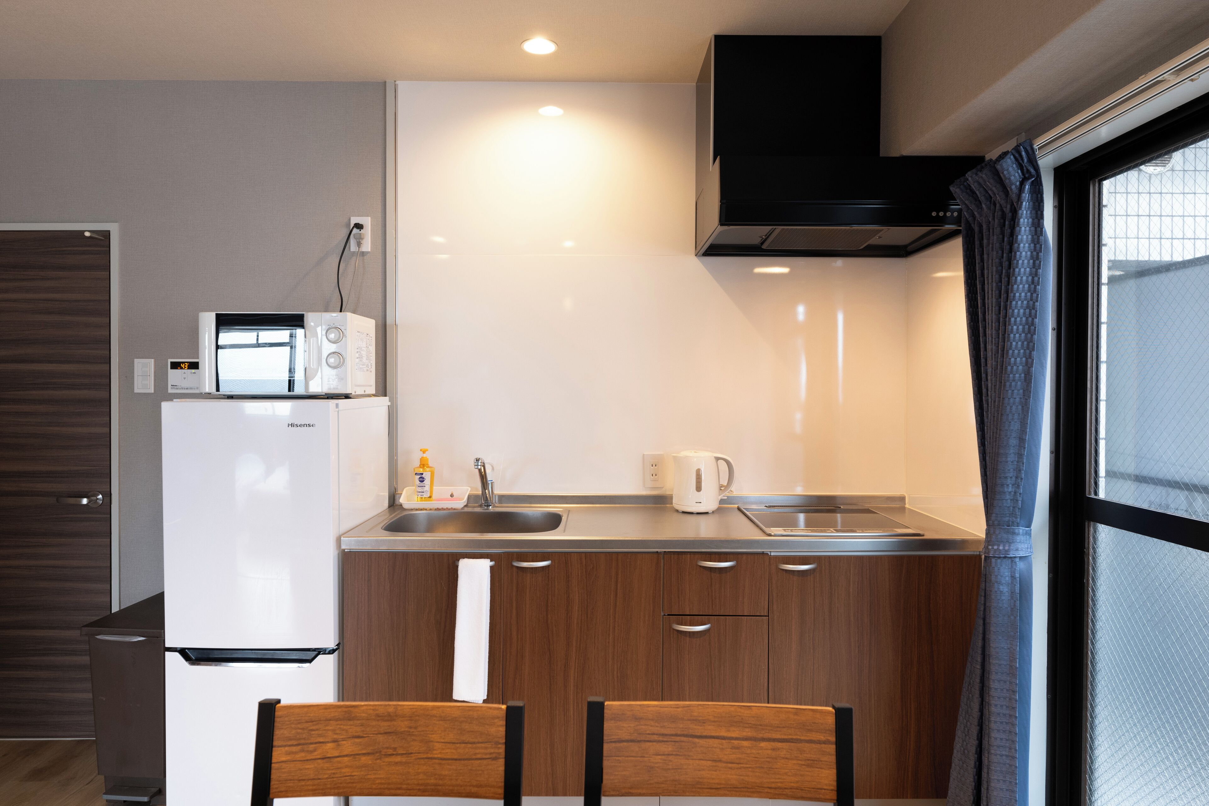 A compact kitchen with a refrigerator, microwave, sink, and a kettle.