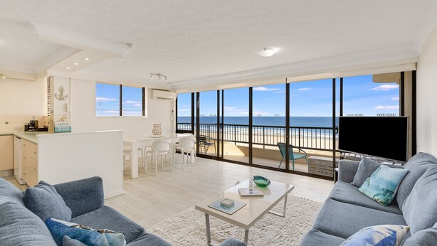 Un vaste espace de vie avec un grand balcon donnant sur la plage, un coin cuisine et un téléviseur à écran plat.