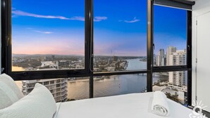 A hotel room with a large window offering a view of a cityscape and a river. - Circle on Cavill 3 Bedroom Ocean View — Q Stay (Surfers Paradise)