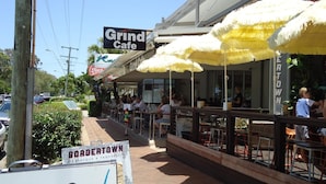 An outdoor dining area with yellow umbrellas, a sign for Grind Cafe, and a sign for Bordertown Barbeque & Taqueria. - Noosaville River Front  - Watch the colors over the water (Noosaville)