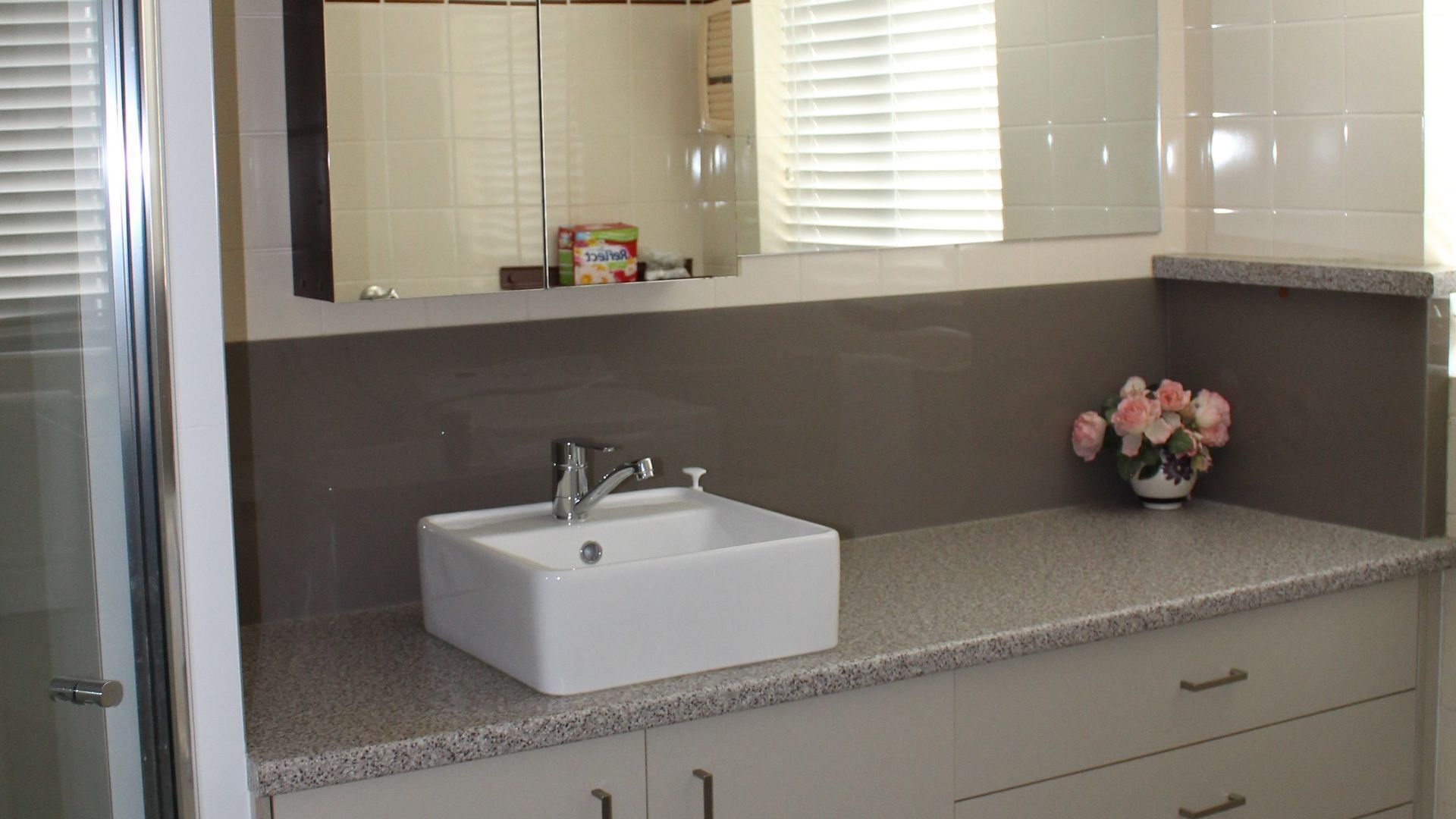 Une salle de bain avec un lavabo blanc, un miroir au-dessus et un vase rempli de fleurs posé sur le comptoir.