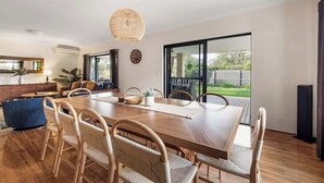 A spacious dining area with a wooden table and wicker chairs, a hanging light fixture, and a view of the outdoors through large glass doors. - Our Escape: Coastal Poolside Haven in Dunsborough (Dunsborough)
