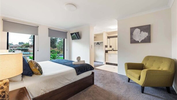 A modern bedroom with a bed, a chair, a TV, and a view of the outside. - Our Escape: Coastal Poolside Haven in Dunsborough (Dunsborough)
