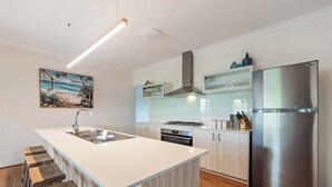 A modern kitchen with a central island, stainless steel appliances, and a wooden bar stool seating area. - Our Escape: Coastal Poolside Haven in Dunsborough (Dunsborough)