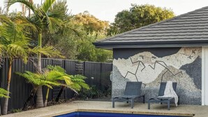 A swimming pool with two lounge chairs, a decorative wall, and a fence with palm trees. - Our Escape: Coastal Poolside Haven in Dunsborough (Dunsborough)