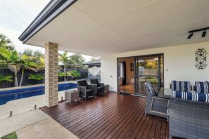 Un espace extérieur abrité comprenant une piscine, des sièges et une porte vitrée donnant accès à un espace intérieur.