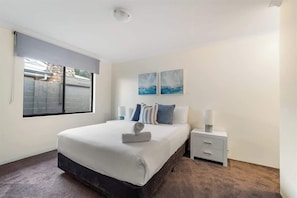 A bedroom with a bed, a nightstand, a lamp, and two wall-mounted paintings.