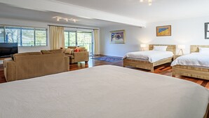 Quarto de hotel com uma cama grande, duas camas menores, um sofá, uma TV e obras de arte nas paredes.