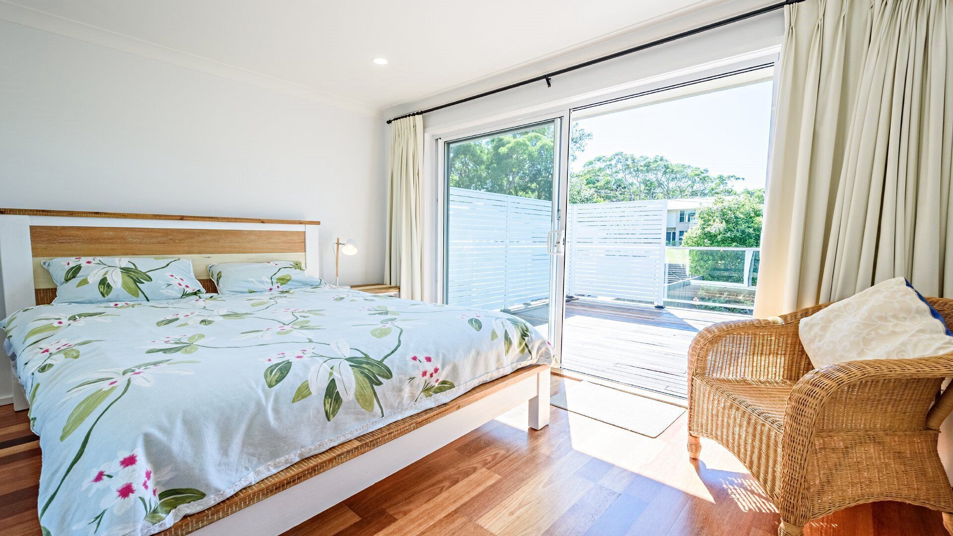 Un dormitorio con una cama, una silla de mimbre y un ventanal corredera que da a un espacio exterior.