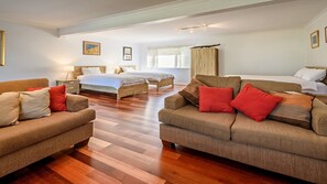 A hotel room with two beds, a sofa, a nightstand, and a window with blinds.