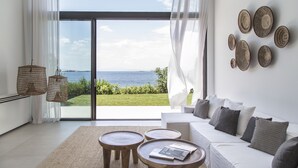 Una sala de estar moderna con un sofá blanco, dos mesitas de madera y vista al mar a través de amplios ventanales.
