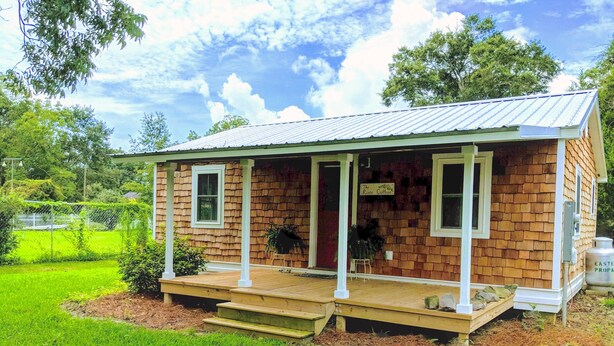 A small, single-story house with a porch, a sign reading "The Rose Cottage," and a brick exterior.