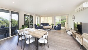 Een ruime woonkamer met een eettafel, stoelen, banken en een televisie.