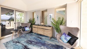 Een moderne woonkamer met een groot raam, een bank, een fauteuil, een houten dressoir en uitzicht op het omliggende landschap.