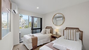 Une chambre d’hôtel avec deux lits, une grande fenêtre donnant sur un beau paysage, un miroir rond et un appareil de climatisation.