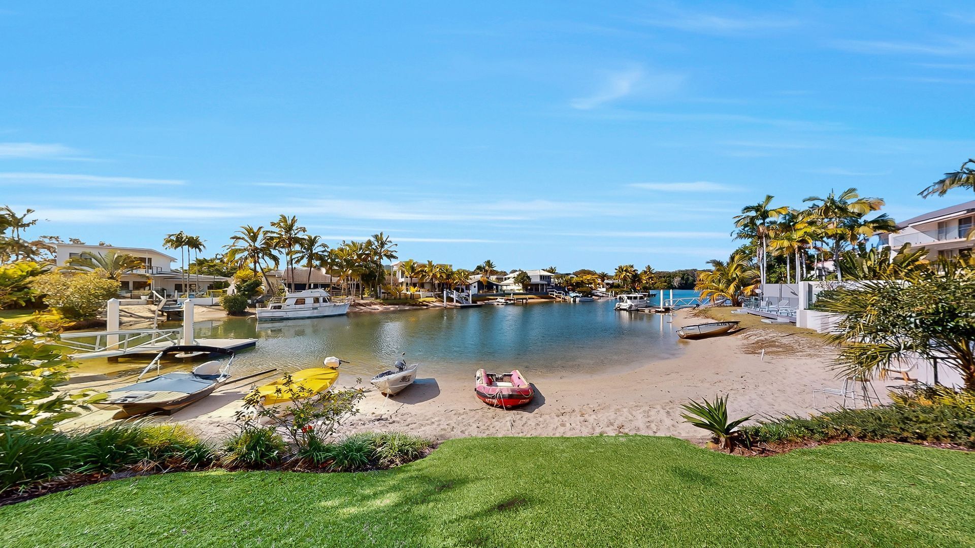 A marina with boats, a sandy beach, and palm trees.