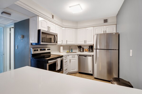 A modern kitchen with white cabinetry, a stainless steel refrigerator, a microwave, an oven, and a dishwasher. - Glamorous Oceanfront (Miami)
