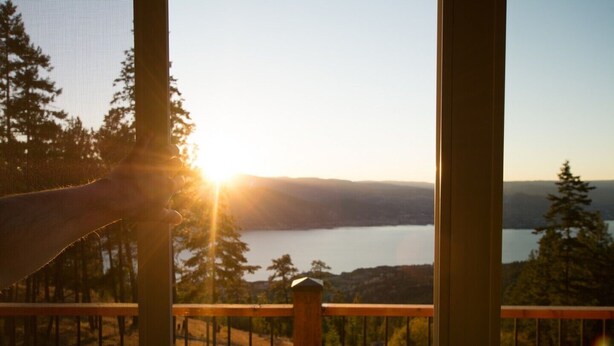 A view from a balcony overlooking a lake with trees and a sunset. - Crooked Tree Guest Suites - The Fir Suite (Penticton)