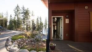 A building with a wooden exterior, a stone pathway leading to the entrance, and a view of a forested area. - Crooked Tree Guest Suites - The Fir Suite (Penticton)