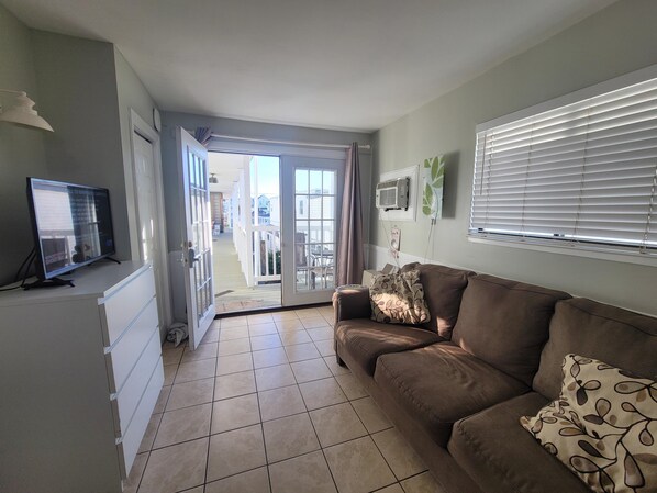 A living room with a brown sofa, a television on a stand, and a sliding glass door leading to an outdoor area.