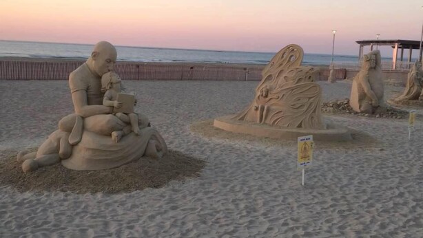 Una spiaggia con sculture di sabbia, tra cui la figura di un uomo e un bambino e una scultura a forma di albero.