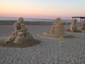 A beach with sand sculptures, including a figure of a man and child, and a tree-like sculpture.