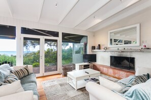 A spacious living room with a fireplace, a television, and a large window overlooking greenery. - The Grove (Lorne)
