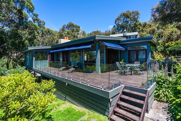 A modern house with a glass-enclosed deck, outdoor furniture, and a wooden staircase.