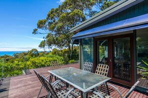 A glass-top table with chairs on an outdoor deck, overlooking a scenic view.
