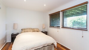 A bedroom with a large bed, two bedside tables, a window with blinds, and a radiator. - The Grove (Lorne)
