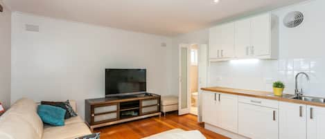 Ein modernes Wohnzimmer mit einer Couch, einem Fernseher und einer Küche mit weißen Schränken und einer Holzarbeitsplatte.
