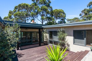 A modern house with a wooden deck, large windows, and a view of trees.